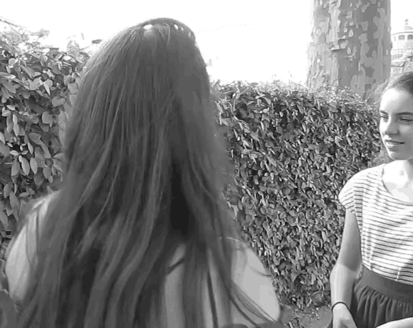 a black and white photo of two girls standing in front of a hedge