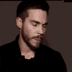 a man with a beard and mustache is wearing a black shirt and making a face .