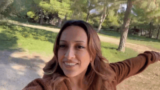 a woman is taking a selfie in a park with her arms outstretched and smiling .