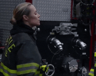 a woman in a fireman 's uniform is standing in front of a fire truck .