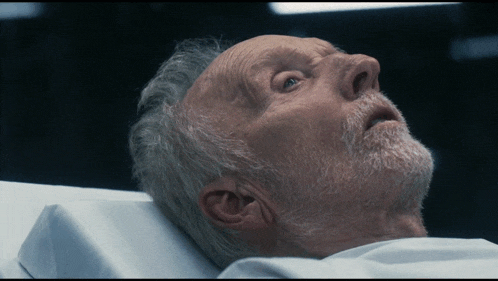 a man with a beard is laying in a hospital bed with his eyes closed