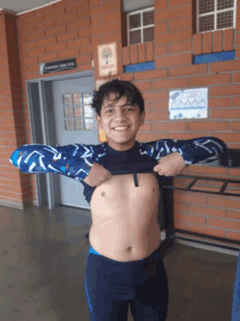 a boy is taking off his shirt in front of a brick wall with a sign that says casa