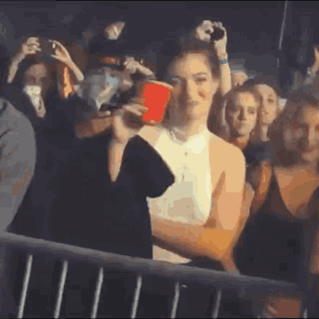 a woman is holding a red cup while standing in a crowd of people .