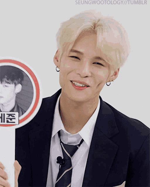 a man in a suit and tie is smiling and holding a sign that says seungwootology tumblr