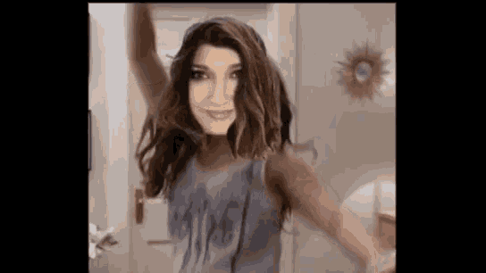 a woman is dancing with her arms in the air while wearing a gray tank top .