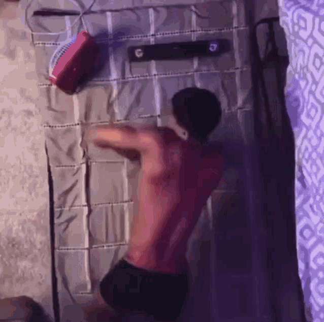 a shirtless man is laying on a bed next to a fan and a speaker .