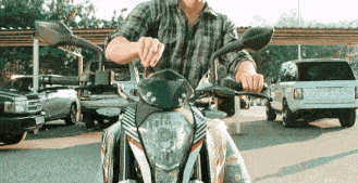 a man in a plaid shirt is riding a motorcycle in a parking lot with a range rover parked behind him