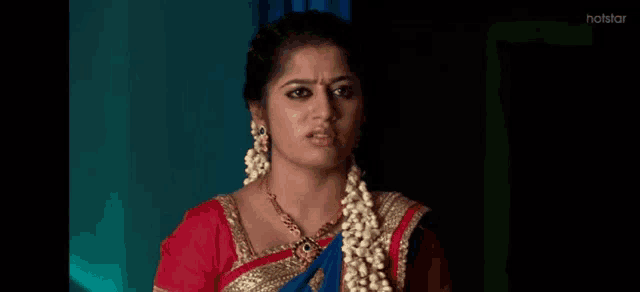 a woman in a red top and a blue saree is making a funny face .