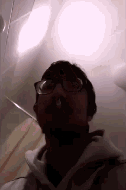 a man wearing glasses and a white hoodie has a drop of liquid coming out of his nose