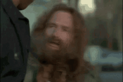 a man with long hair and a beard is standing next to another man and talking to him .