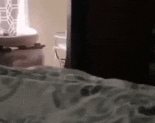 a person is standing in a bedroom next to a bed and a sink .