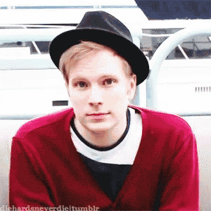 a young man wearing a black hat and a red sweater is looking at the camera