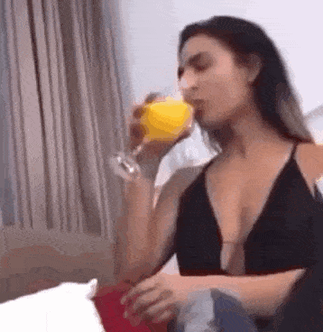 a woman in a black tank top is drinking orange juice from a glass .