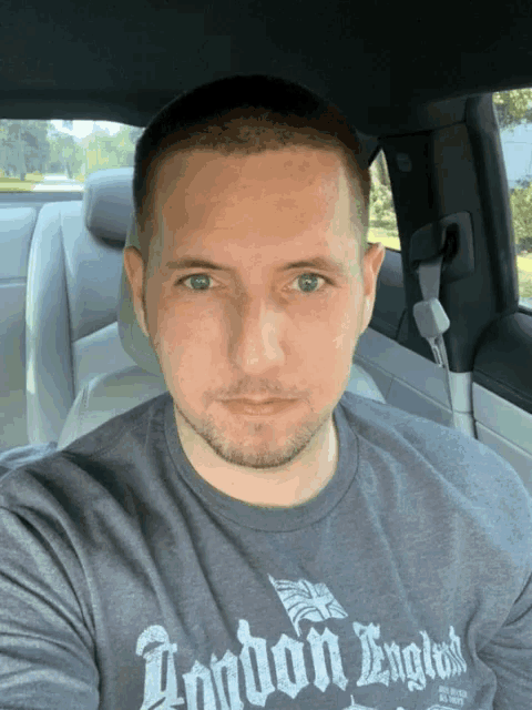 a man wearing a london england t-shirt is sitting in a car