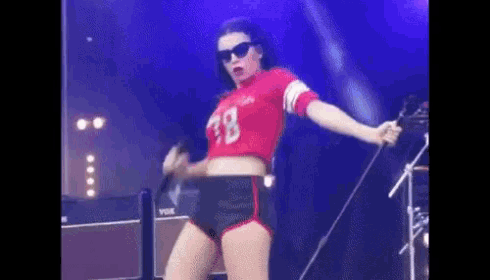 a woman in a red crop top and black shorts is singing into a microphone .