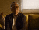 an elderly man wearing glasses is sitting on a yellow couch in a dark room .