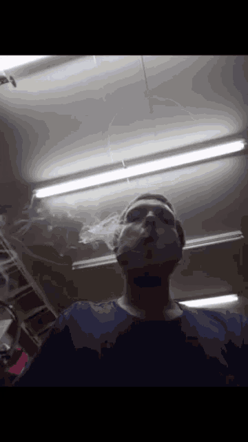 a man in a blue shirt is smoking a cigarette in a dark room