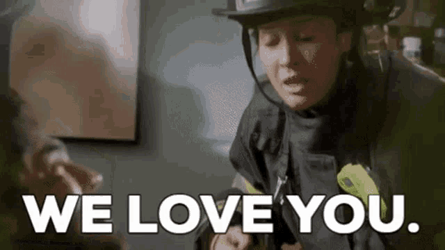 a woman in a firefighter 's uniform is holding a man 's hand and saying `` we love you . ''