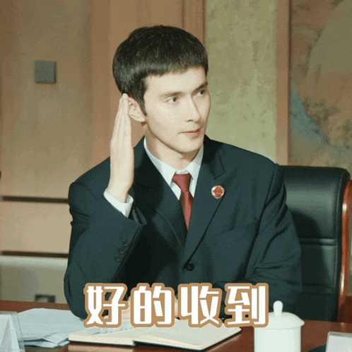 a man in a suit and tie is sitting at a desk with chinese writing on the top