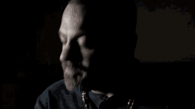 a man with a beard is sitting in the dark with the words `` bullsh * t '' written on the screen .