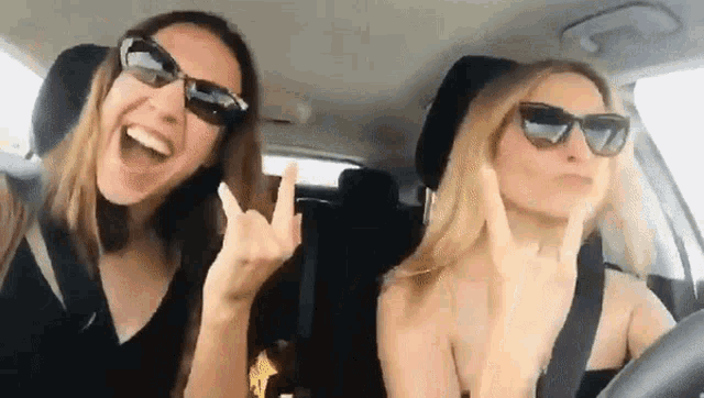 two women wearing sunglasses are sitting in a car making funny faces