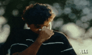 a man wipes his nose with a tissue and the word xhk is on the bottom of the image