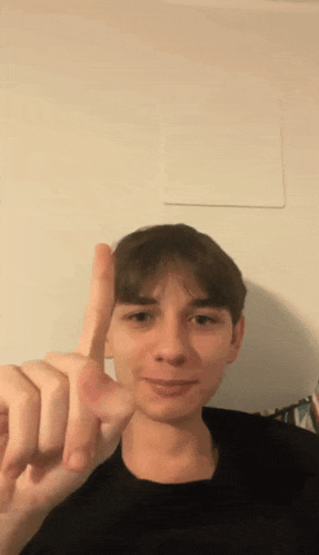 a young man in a black shirt is pointing up with his finger