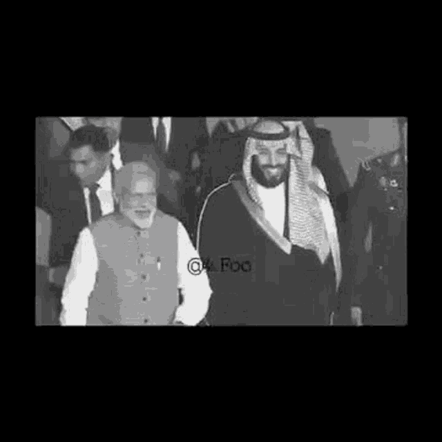 a black and white photo of a man in a keffiyeh walking with a man in a suit .