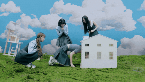 three girls are playing with a small white house in a field