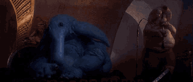 a blue monster with a long nose is sitting next to a statue of a man