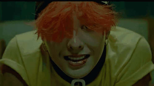 a close up of a person with red hair wearing a yellow shirt and a black choker with the letter c on it