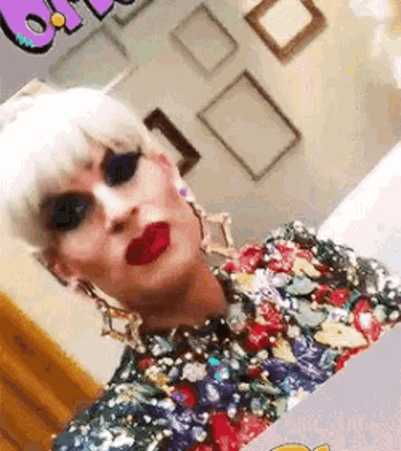 a drag queen is taking a selfie in front of a mirror while wearing a colorful dress .
