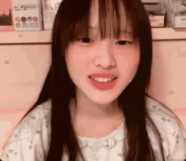 a young girl with long black hair and bangs is smiling and looking at the camera .