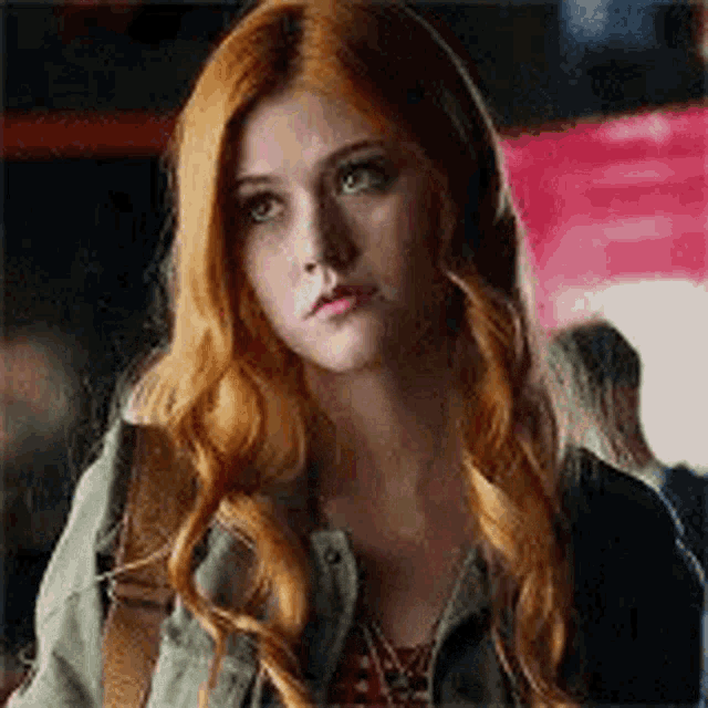 a close up of a woman with red hair wearing a green jacket and a backpack .