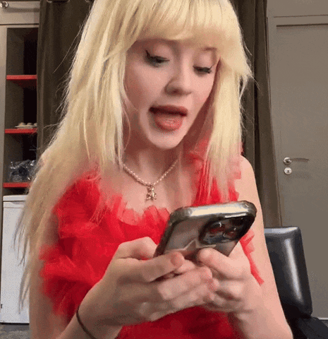 a blonde woman wearing a red dress is looking at her phone