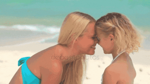 a woman and a little girl touching their foreheads on a beach