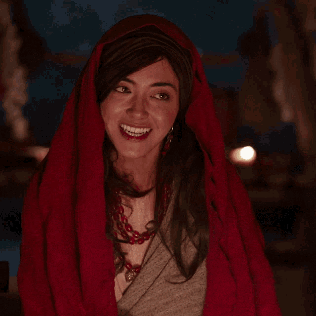 a woman with a red scarf around her head smiles with her eyes closed