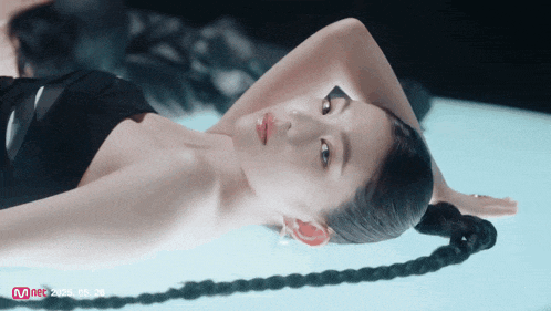 a woman in a black dress is laying on a blue surface with a mnet logo in the corner