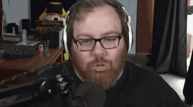 a man with a beard and glasses is wearing headphones and talking into a microphone