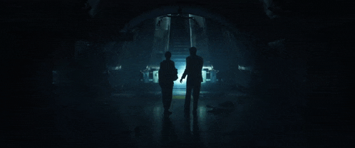 two people are walking through a dark room with a light shining on them