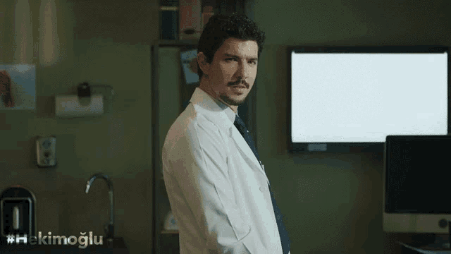 a man in a lab coat stands in front of a monitor with the hashtag #hekinoglu