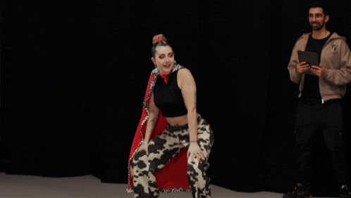 a woman in cow print pants and a red cape is dancing