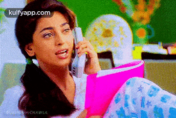 a woman is talking on a cell phone and holding a pink book .