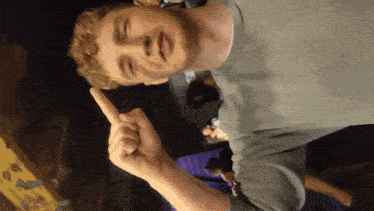 a man in a grey shirt is making a funny face with his finger up
