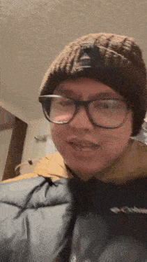 a man wearing glasses and a beanie is standing in a room .