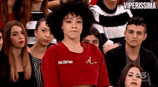 a woman is sitting in a crowd of people wearing a red crop top .
