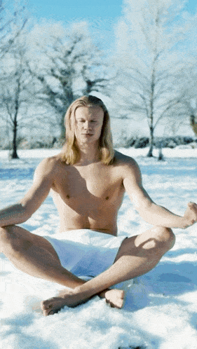 a shirtless man sits in a lotus position in the snow with his legs crossed