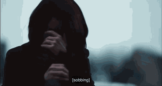 a woman in a hood is covering her face with her hands and the word sobbing is visible in the corner