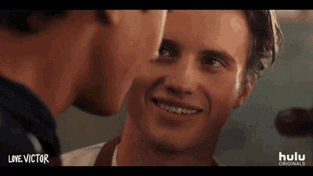 two young men are smiling at each other and looking at each other 's faces .