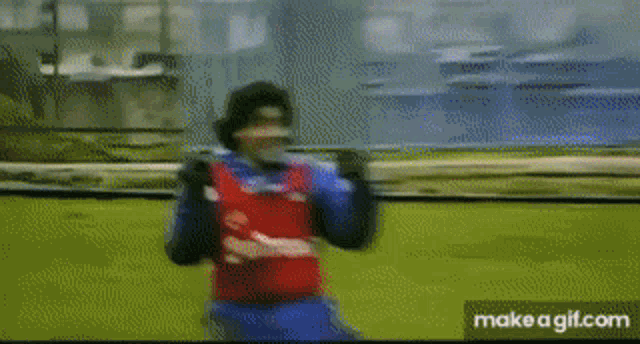 a man in a red and blue jersey is standing on a field with his arms in the air .